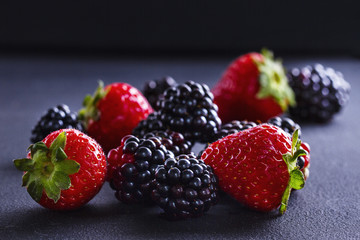 Strawberries and blackberries on a black table, closeup