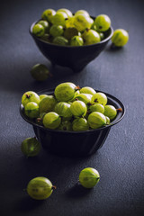 Two bowls full of gooseberries on black