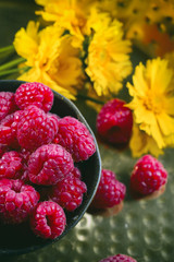 Ripe raspberries in a bowl and yellow flowers on golden background