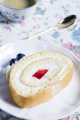 A slice of fruity roll cake and a cup of coffee on floral tablecloth