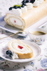 Fruity roll cake and cup of fresh coffee on floral tablecloth