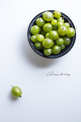 Fresh gooseberries in a metal bowl on white background with copyspace