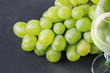 White grapes wine in a glass and fresh grapes on black