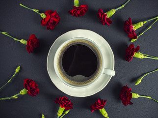 Red carnations and a cup of coffee on black table, closeup