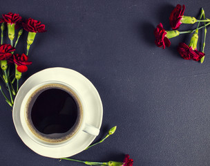 A cup of coffee and red carnations on black table with space for text