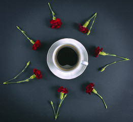 A cup of coffe and carnations on black table, view from top