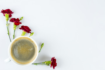 A cup of coffee and red carnations on white with space for text, view from top