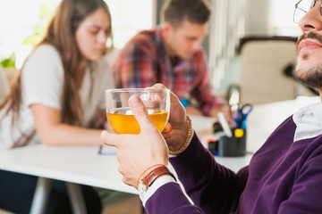 Young businessman drinks tea while his collegues on background work hard.