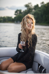 Portrait of attractive woman relaxing on yacht enjoying glass of wine on blue sky sea outdoors. Enjoyment and luxury lifestyle