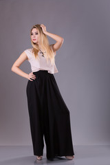 Fototapeta premium Young blond woman in white shirt, black pants, and high heels standing with hand on head.