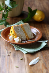 Piece of Angel Food Cake with Lemon Curd decorated with pistachios and white chocolate leaves, on brown plate, on wooden table.