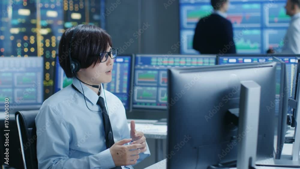 Poster In the Network Operations Center Trader Makes Personal Client Call with a Headset. In the Background Traders Discuss Data Shown on Monitors. Shot on RED EPIC-W 8K Helium Cinema Camera.