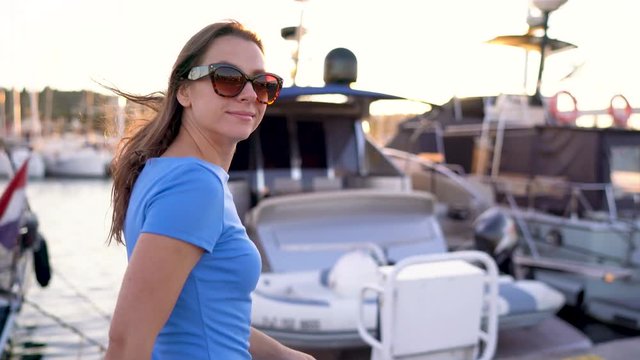 Woman in sunglasses walking along the dock with a lot of yachts and boats at sunset, close up