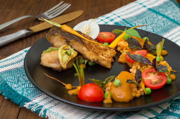 Dish from fried fish with lentils, green peas, apricot sauce, baby carrots and cherry tomatoes. Wooden background. Close-up. Top view