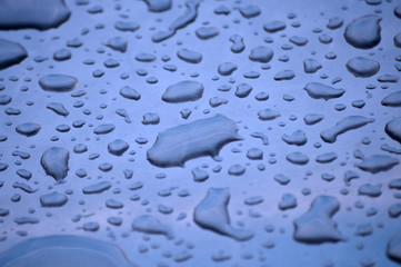 Wassertropfen auf einer polierten Metalloberfläche in bläulichem Licht
