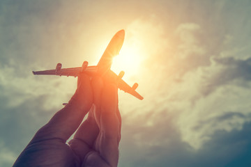 Obraz premium ręka trzyma model samolotu przed pochmurnego nieba tle. koncepcja transportu lotniczego.
