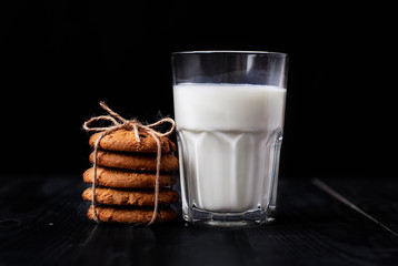 Oatmeal cookies with raisins and a glass of milk for a healthy breakfast on a black background.