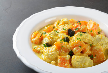 Baked pumpkin with chicken and cream sauce in a white plate on a dark stone background, closeup