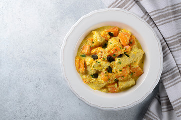 Baked pumpkin with chicken and cream sauce in a white plate on a light stone background, served with napkin, top view