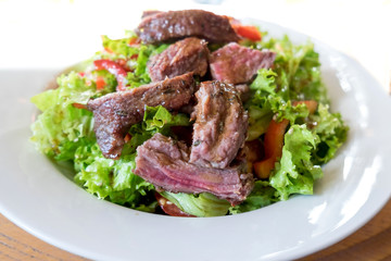 Veal steak salad with arugula, lettuce, halfs of small cherry tomatoes, stripes of sweet pepper and toasted bread