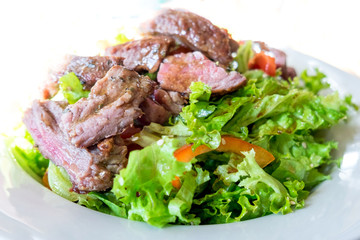 Veal steak salad with arugula, lettuce, halfs of small cherry tomatoes, stripes of sweet pepper and toasted bread