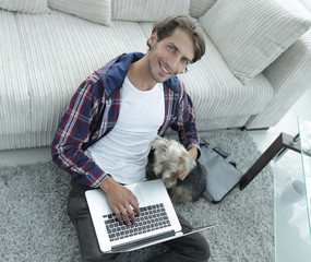 handsome guy with laptop hugging his dog and sitting near the couch
