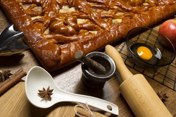 Apple pie with baking ingredients, spices and kitchen tools for cooking, rustic homemade sweet food on wooden table, selective focus 