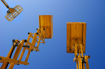 Scissor lift platform, cherry picker, aerial platform with bucket, three yellow construction machines and cranes, heavy industry, blue sky on background, bottom view  - 176297875