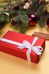 Christmas background with red gift box, fir tree branches with glass balls, pine cones and cinnamon sticks  on golden background, free space. Red luxury New Year gift, copy space