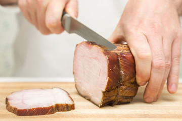 Chef's hands with knife cutting a smoked ham on the wooden board for sandwich, italian pizza or snack in the kitchen. Preparation for cooking. Healthy eating and lifestyle. Food concept.