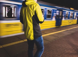 Samotna osoba w żółtej kurtce czeka wieczorem na pociąg na pustym peronie    - obrazy, fototapety, plakaty