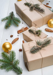 Fototapeta na wymiar Christmas background with gift boxes wrapped in kraft paper, fir tree branches, golden glass balls, pine cones, cinnamon sticks and stars anise on white wooden background