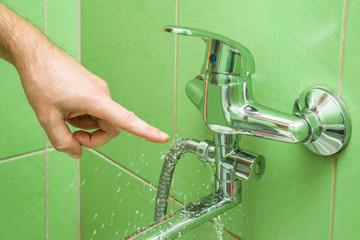 Man's hand finger pointing to a damaged leaking water tap hose in the bathroom of house, flat or other place. Plumbing concept. - obrazy, fototapety, plakaty