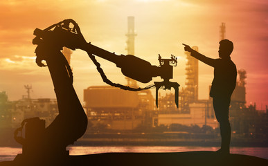 Industry 4.0 technology , artificial intelligence trend concept. Silhouette of business man point finger forward to heavy automation robot arm machine. Vivid sunset sky and smart factory background.