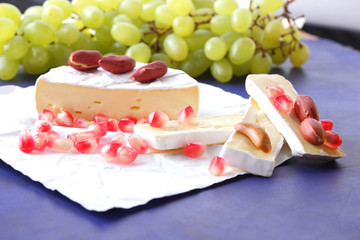 Camembert cheese, sliced cheese, soft cheese with mold, green grapes, peanuts and pomegranate seeds on a dark blue background