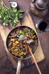 Fresh fried veal liver with chanterelle and baguette in sauce as top view in a casserole