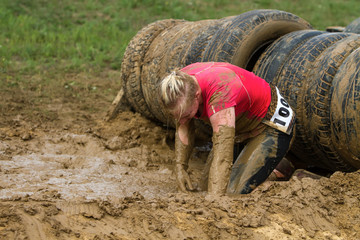 The girl creeps in the mud, emotionally overcoming the obstacle made of tires.