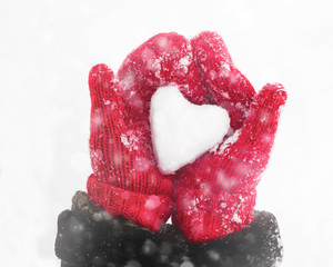 Female hands in knitted mittens with heart of snow in winter day. Love concept. Valentine day...