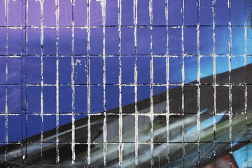 The wall of a residential house, covered with tiles and painted with blue and black paint. Part of...