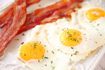 latter with bacon strips and fried eggs topped with black pepper and fresh chives