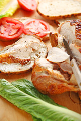 Cutting roast chicken into slices for sandwiches with lettuce and tomatoes
