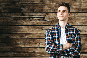 Happy attractive young man in plaid shirt standing and smiling over wooden background