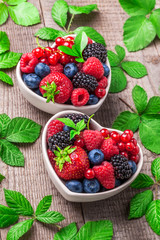 Berries overhead with leaves colorful closeup assorted mix in heart shaped ceramic jars. Raspberry, blueberry, red currant, strawberry on rustic wooden table in studio.