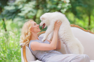 Beautiful young girl with a white puppy in her arms on a retro sofa in a summer garden