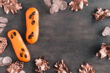 Two orange glazed eclairs and gold colored leaves on dark background. Stylish fall season flatlay. Copy space for text