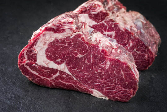 Two raw dry aged Kobe rib eye steak as close-up on a black board