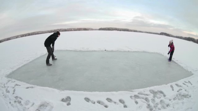 Playing hockey on cleared rink on ice of big lake, father and son