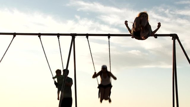 Slow motion of unrecognizable people swinging high on swing set outside on bright summer day.