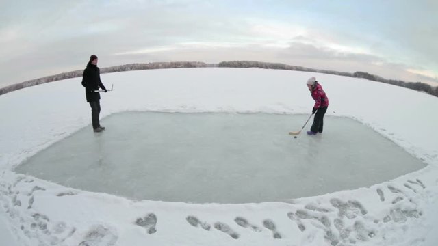 Winter pleasure with ice hockey sticks on icy ground on lake, family with man and child