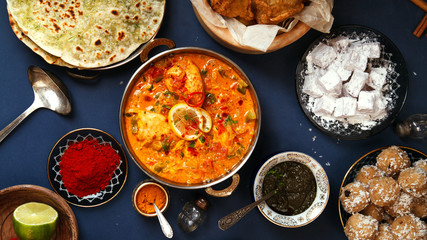 Indian cuisine on diwali holiday: tikka masala, samosa, patties and sweets with mint chutney and spices. Dark blue background. Banner composition